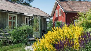 Two wooden houses with red and white exteriors, surrounded by lush greenery and vibrant yellow flowers. - Nachhaltig und gefühlvoll in Seenähe by Interhome (Gnesta)