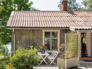 En stuga byggd av trä med ett tak täckt av takpannor, en liten veranda med ett bord och stolar samt ett fönster med utsikt över den omgivande naturen.