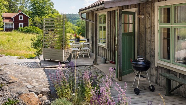 A wooden cabin with a green door, a barbecue grill, and a deck with chairs. - Nachhaltig und gefühlvoll in Seenähe by Interhome (Gnesta)
