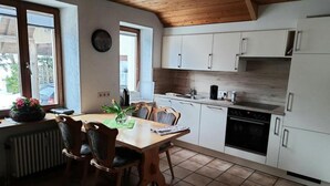 A compact kitchen with white cabinets, a wooden dining table with chairs, and a window providing natural light. - Apartment Ebser by Interhome (Todtnau)