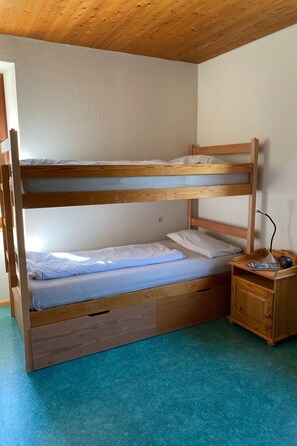 Ein Stockbett mit Holzrahmen, ein kleiner Nachttisch mit Lampe und eine Schublade.