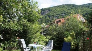 A patio with a table and chairs, surrounded by lush greenery and a mountainous backdrop. - Apartment Ebser by Interhome (Todtnau)