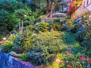 Un jardin luxuriant, avec une variété de plantes et de fleurs, un mur de pierre et un escalier menant à un bâtiment.