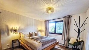 A bedroom with a large bed, two bedside lamps, a window with curtains, a coat rack, and a fur rug. - Schwarzwald Königin by Interhome (Bühlertal)