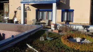 Un bâtiment à deux étages doté d’un balcon, d’un espace extérieur aménagé pour s’asseoir et d’un jardin agrémenté de sculptures.