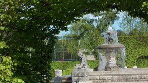Un parc avec une fontaine, des statues en pierre et un banc.