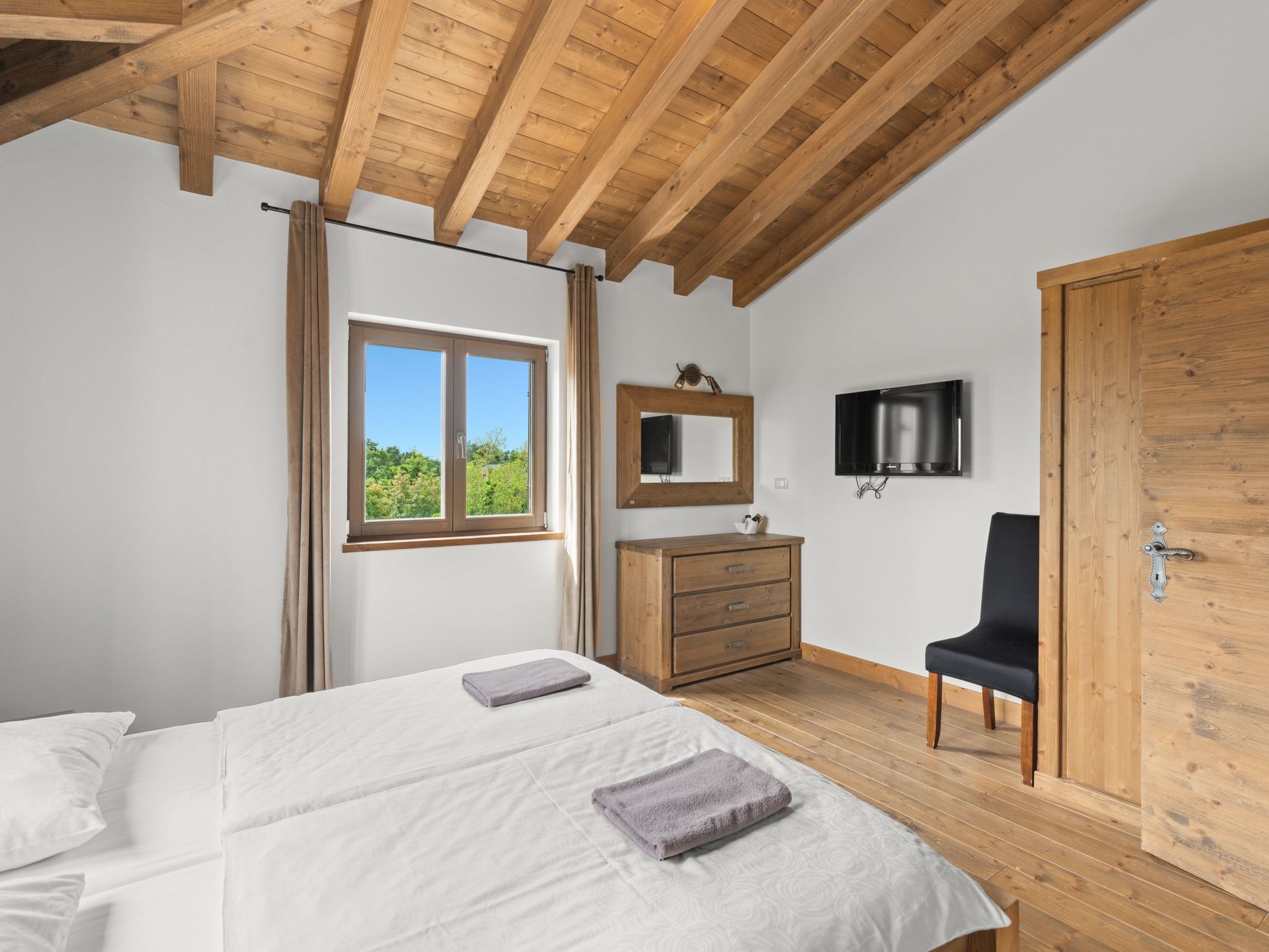 Een slaapkamer met twee bedden, een houten kledingkast, een spiegel, een televisie en een deur.