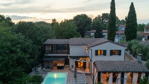 Una casa moderna de dos pisos con piscina, mobiliario exterior y un patio cubierto.