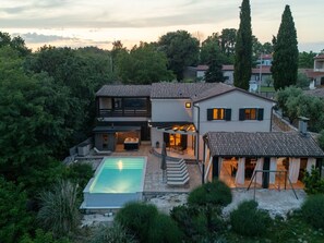 Ein modernes, zweistöckiges Haus mit Swimmingpool, Sitzgelegenheiten im Freien und einer überdachten Terrasse.