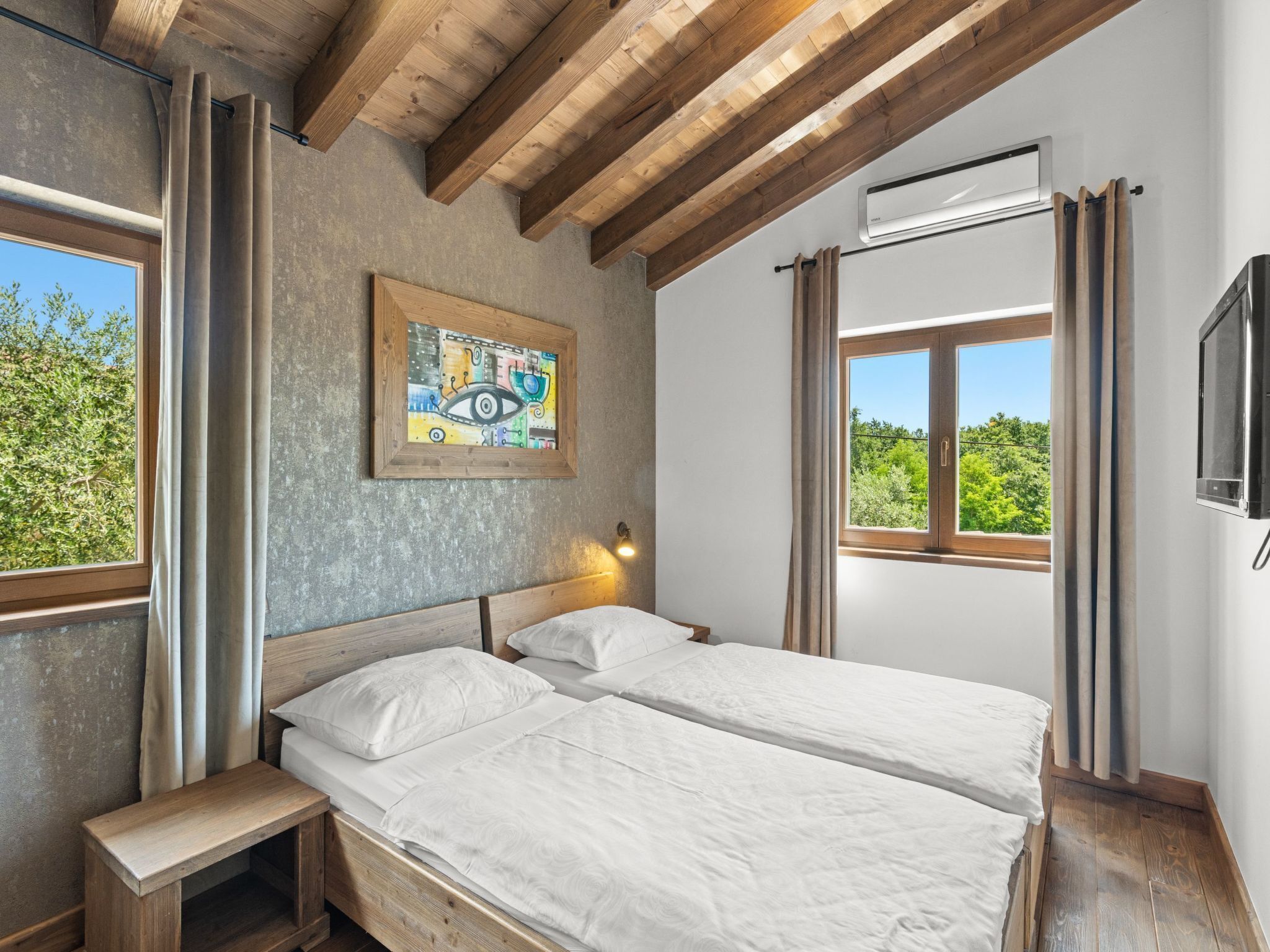 Une chambre avec deux lits, des poutres en bois, un tableau, une fenêtre et un appareil de climatisation.