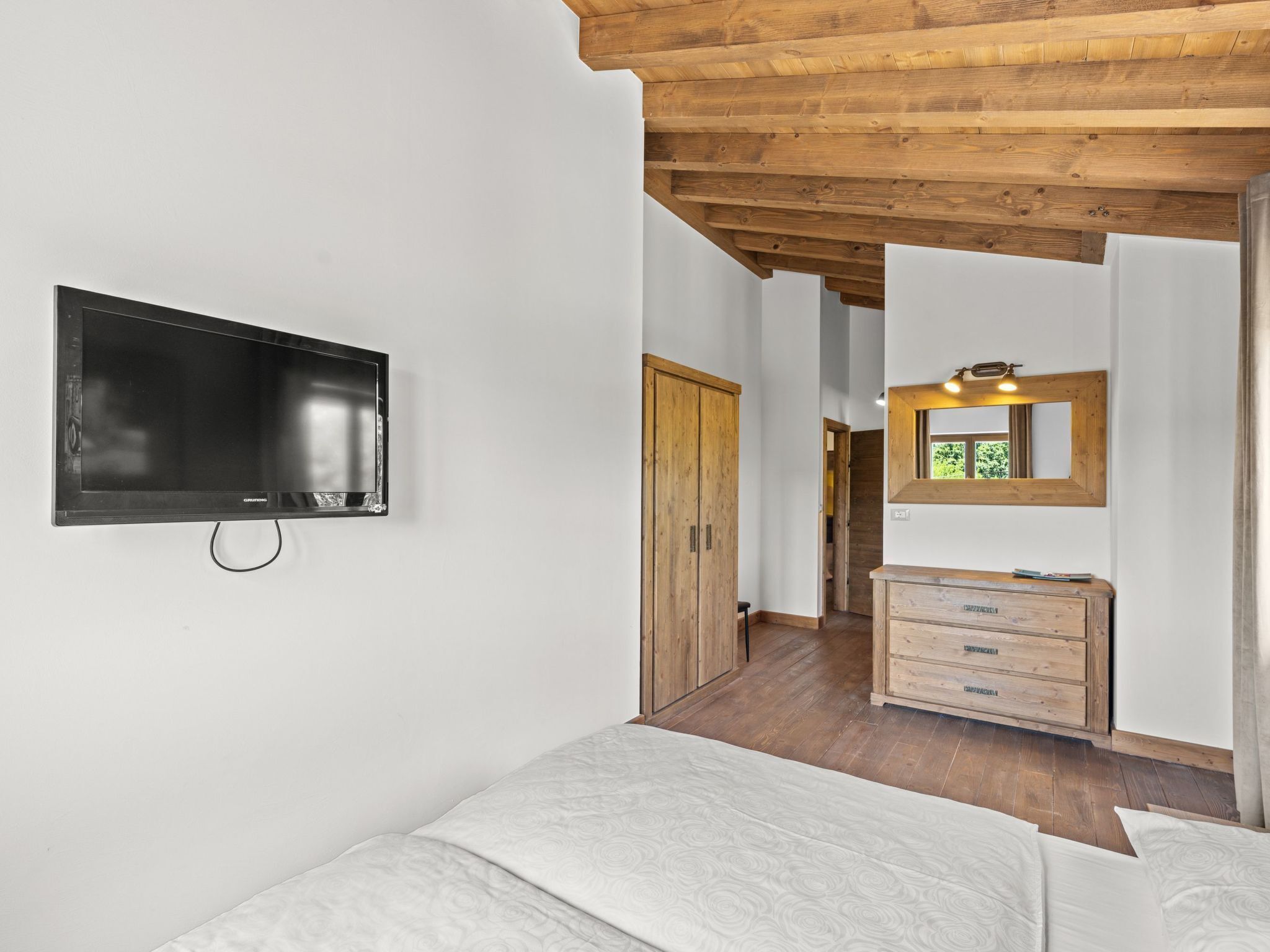 Une chambre à coucher avec un lit, un plafond en bois, une télévision, une commode et un miroir.