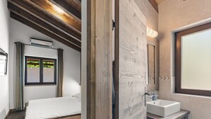 Un dormitorio con cama de madera, ventana con vistas y baño con lavabo y espejo.