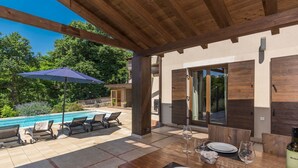 Un patio exterior con piscina, sillones de descanso y una mesa de comedor para dos.