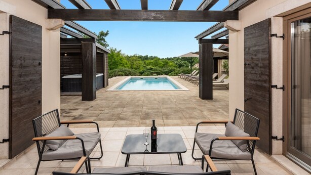 Uma área externa coberta com piscina, espreguiçadeiras e uma mesa.
