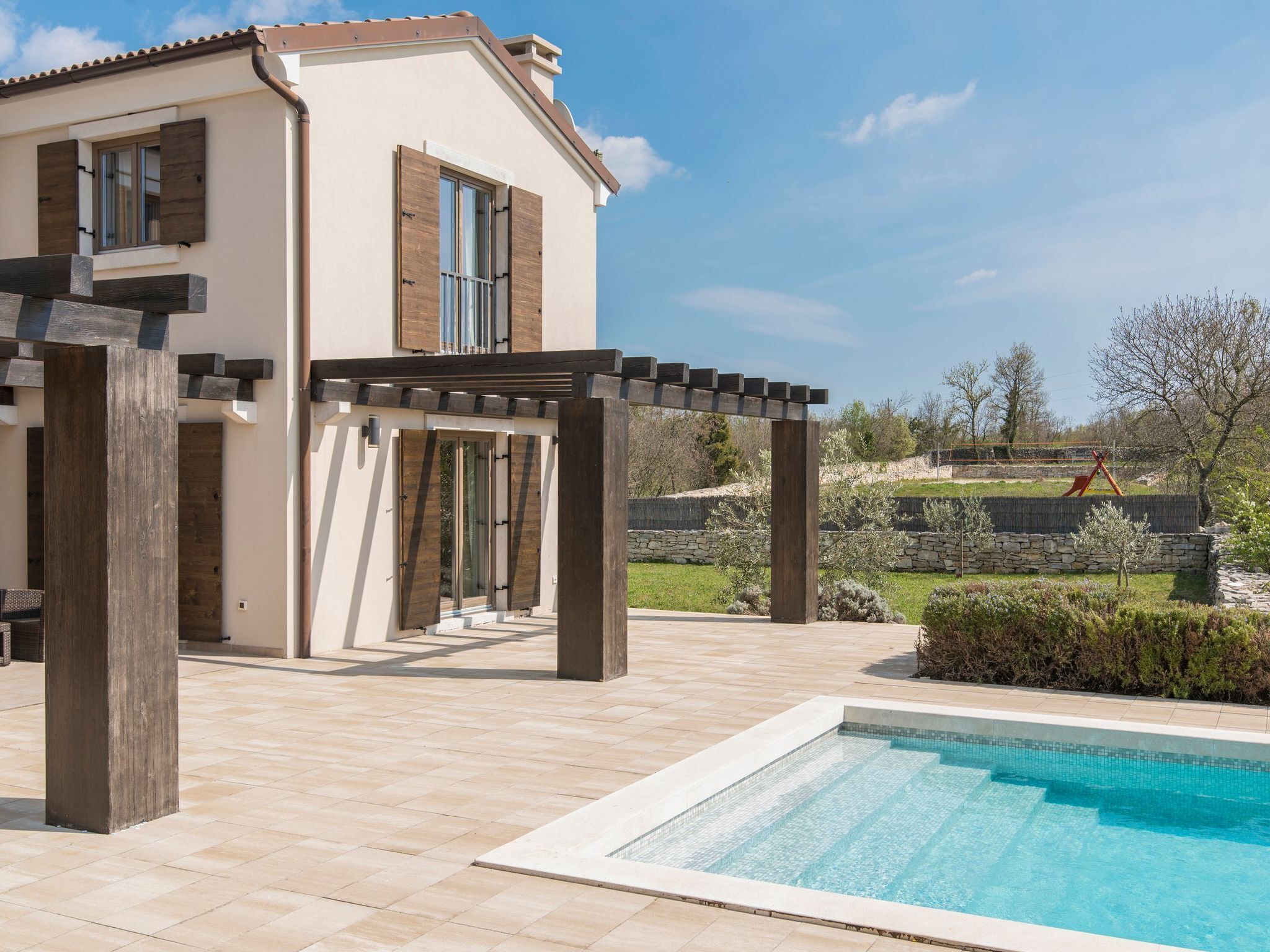 Una casa moderna con piscina, pérgola de madera y paredes de piedra.