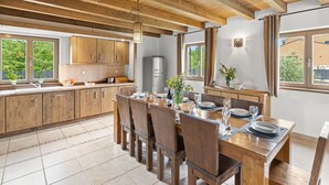 Uma cozinha espaçosa com armários de madeira, uma área de jantar com uma mesa grande posta para seis pessoas e vista para o verde lá fora.