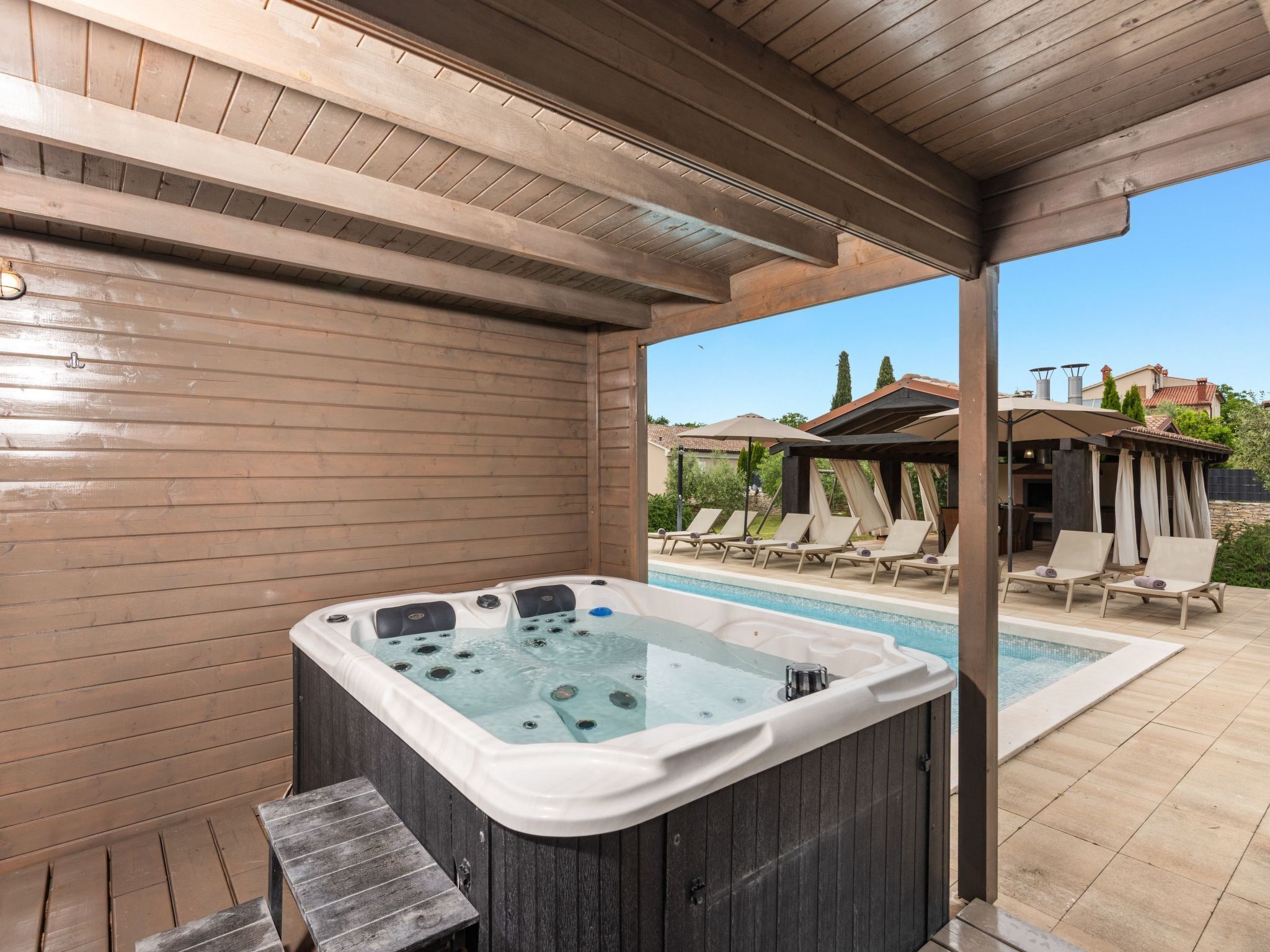 Ein Whirlpool in einem überdachten Außenbereich mit Pool und Liegestühlen.