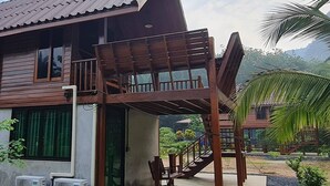Una casa de madera con balcón, equipos de aire acondicionado y una escalera que lleva a un segundo nivel.