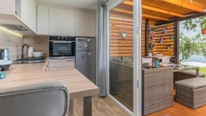 Eine moderne Küche mit Essbereich, Glastüren, die zu einem Außenbereich mit Holzboden und Blumentöpfen führen.