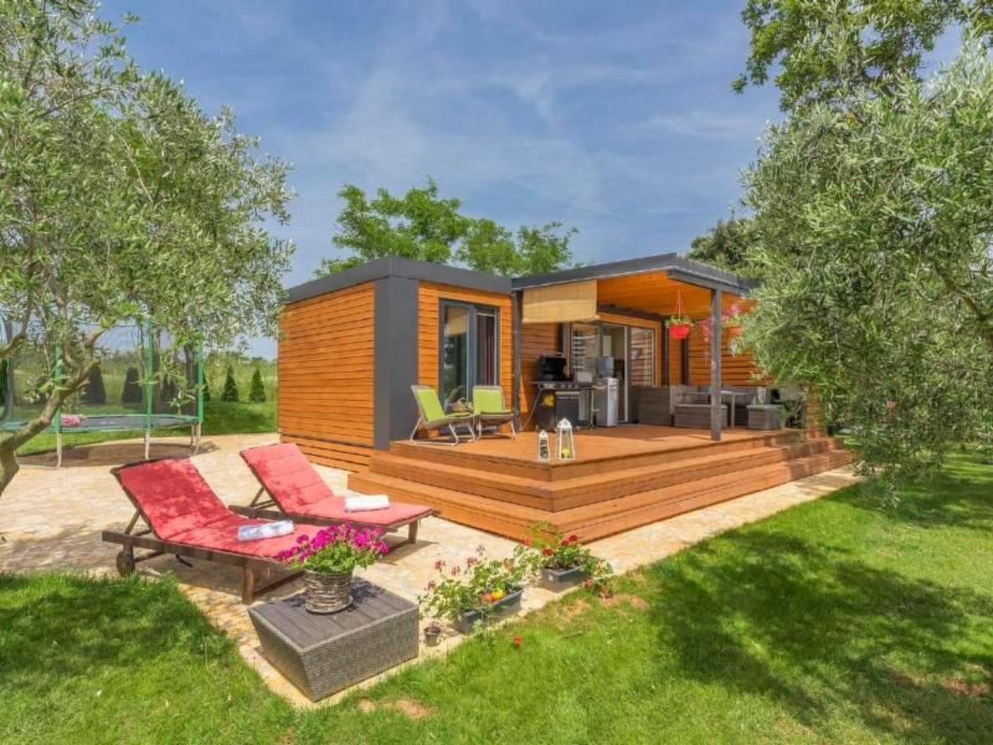 A modern outdoor living area with a wooden deck, lounge chairs, and a barbecue grill.