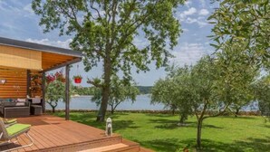 Eine Holzterrasse mit Gartenmöbeln, Blick auf einen See und eine Rasenfläche mit Bäumen.