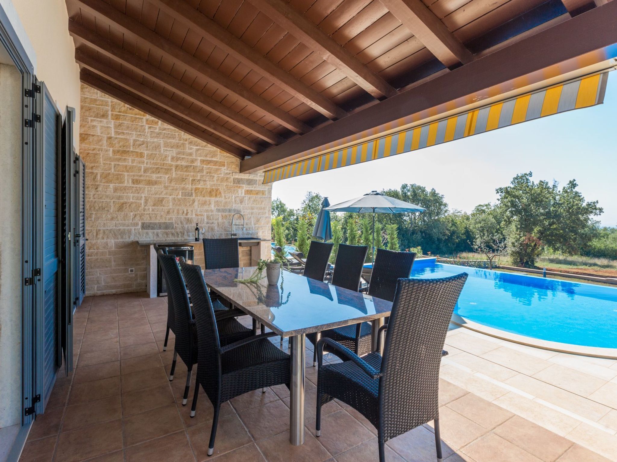 An outdoor patio with a glass table and chairs, a stone wall, and a pool.