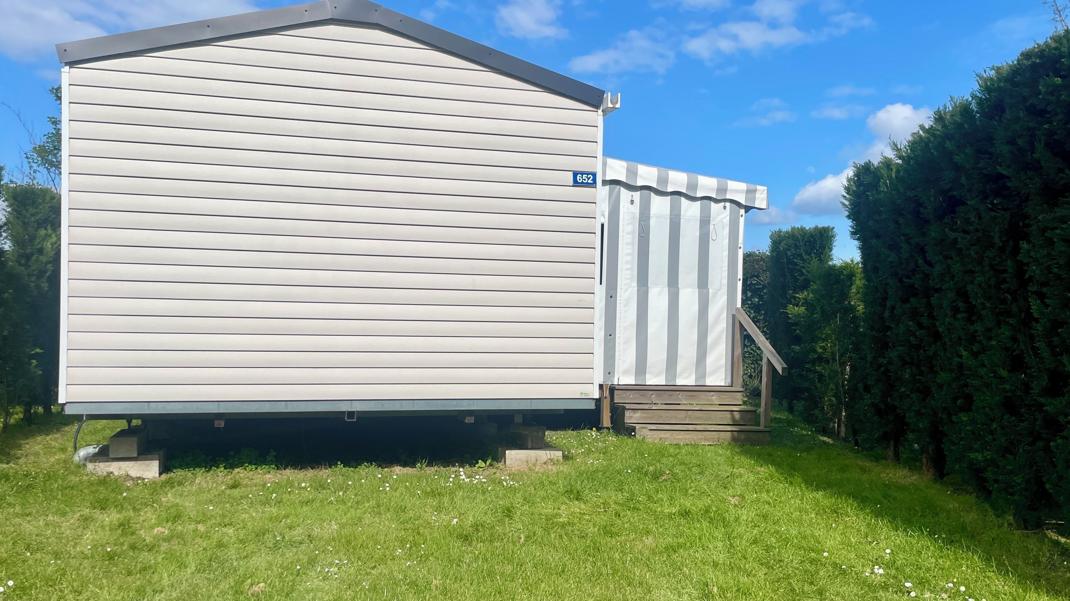 A single-story, light-colored shed with a flat roof, a blue number '652' sign, and a small wooden staircase leading to a door.