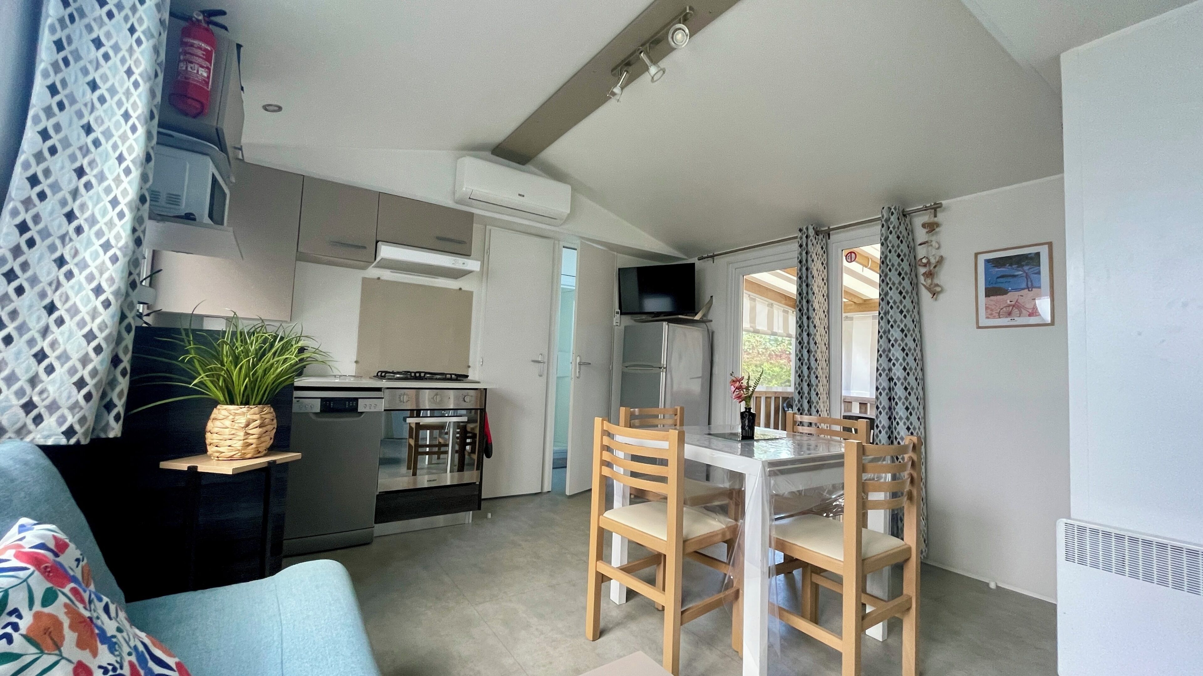 Une cuisine compacte équipée d’une cuisinière, d’un four et d’un réfrigérateur, un coin repas avec une table et des chaises, et un espace de vie avec un canapé et une plante.