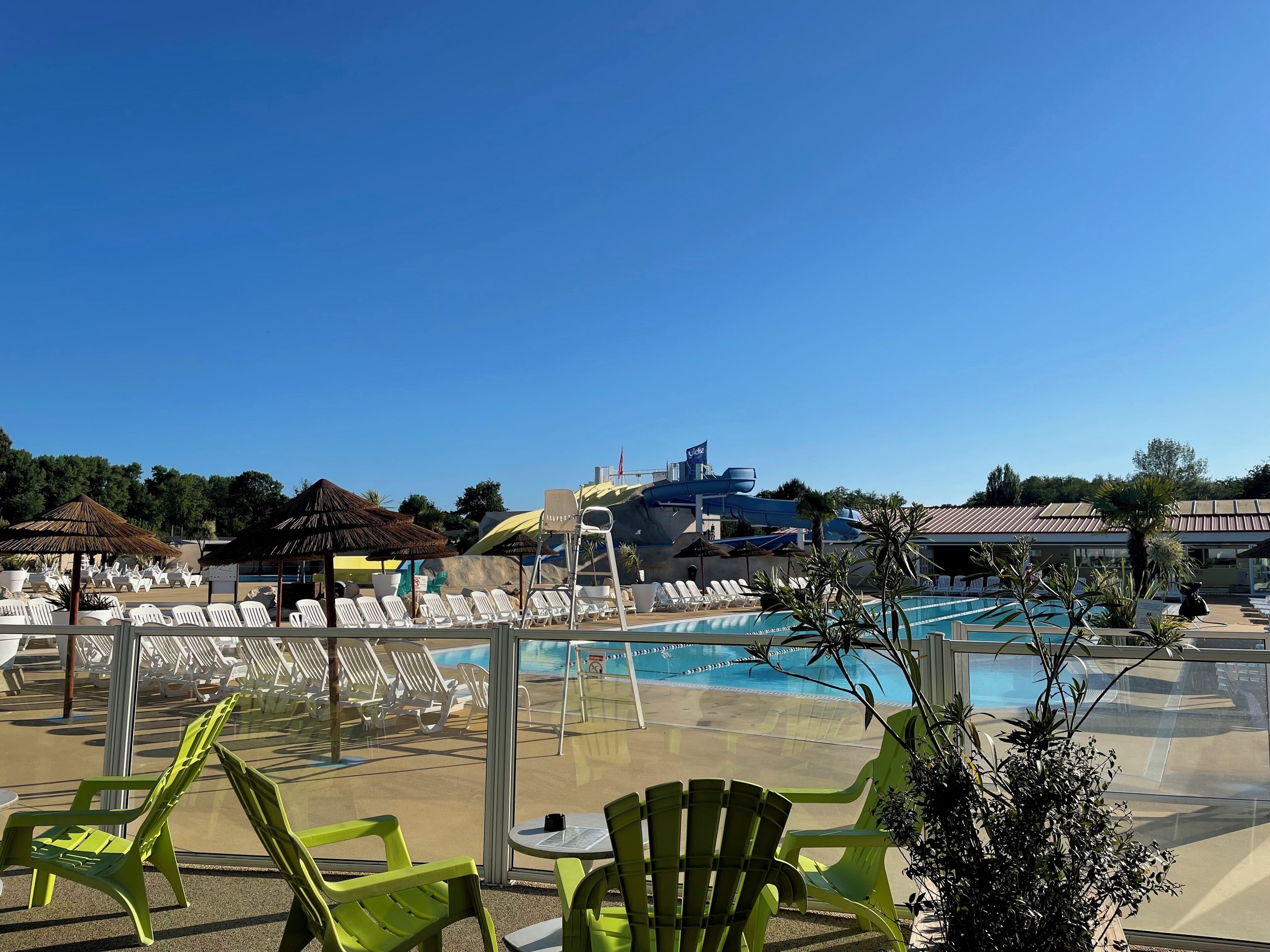 Un espace piscine avec des chaises longues, une table et un toboggan aquatique en arrière-plan.
