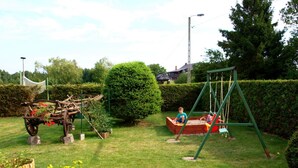 Un jardin avec une balançoire, une petite charrette en bois et une haie.