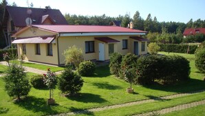 Une maison à deux étages, avec un toit rouge, entourée d’une pelouse et d’un jardin bien entretenus.