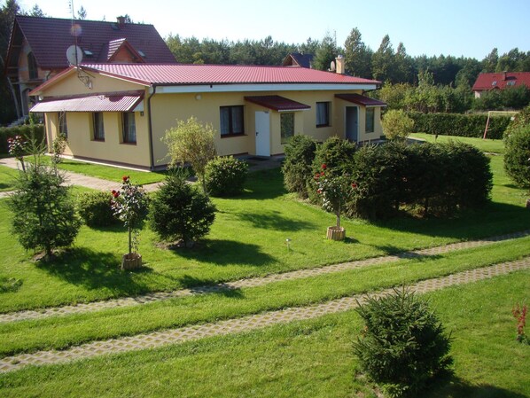 A two-story house with a red roof, surrounded by a well-maintained lawn and garden.