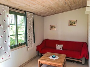 A room with a red sofa, a wooden table with a blue object, and two framed pictures on the wall. - Schwedisches Holzhaus mit Grill und Terrasse by Interhome (Arvidsjaur)