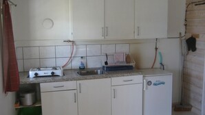 Cocina compacta con muebles blancos, estufa a gas, pileta y refrigerador.