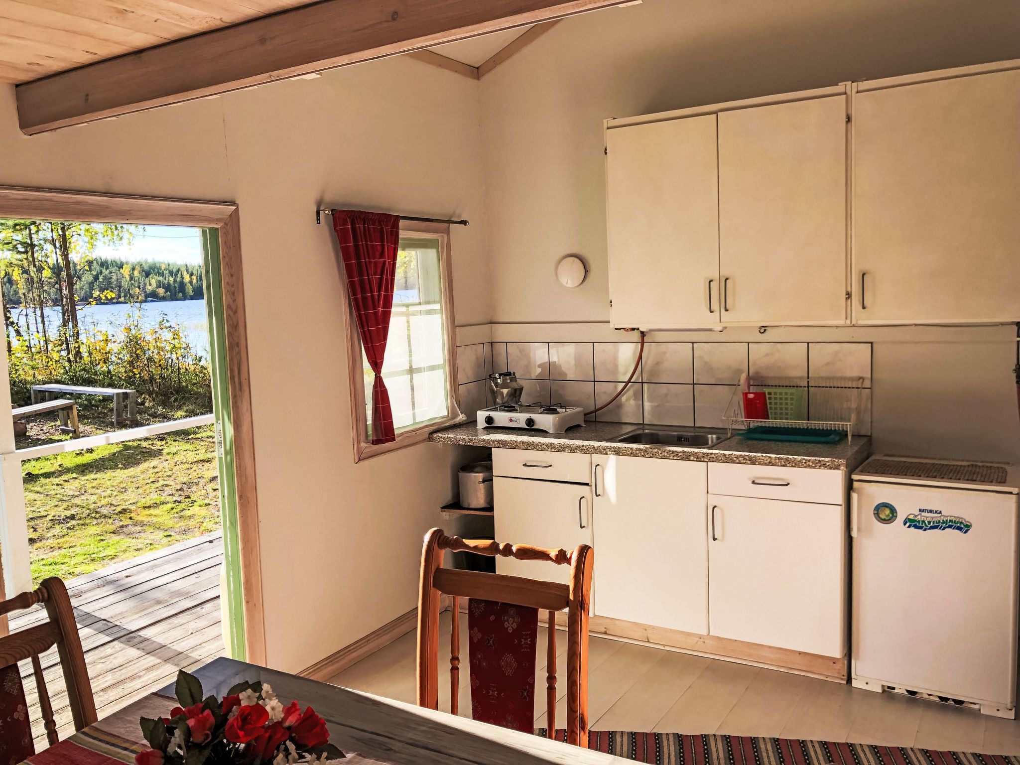 Une cuisine compacte avec vue sur un lac, un coin repas avec une table et des chaises, et un petit réfrigérateur.
