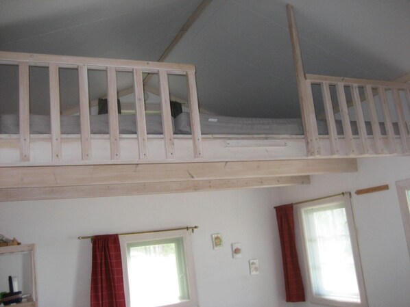 A room with a bunk bed, two windows with curtains, and a small shelf with items.