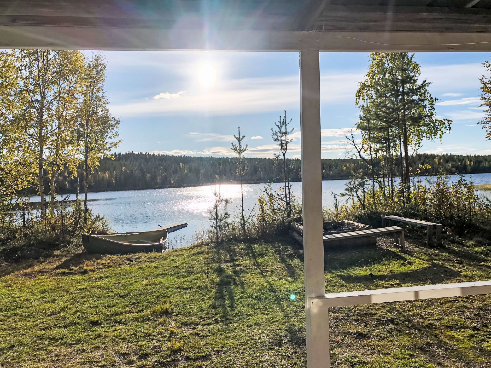 A lakeside view from a covered area with a boat and benches.