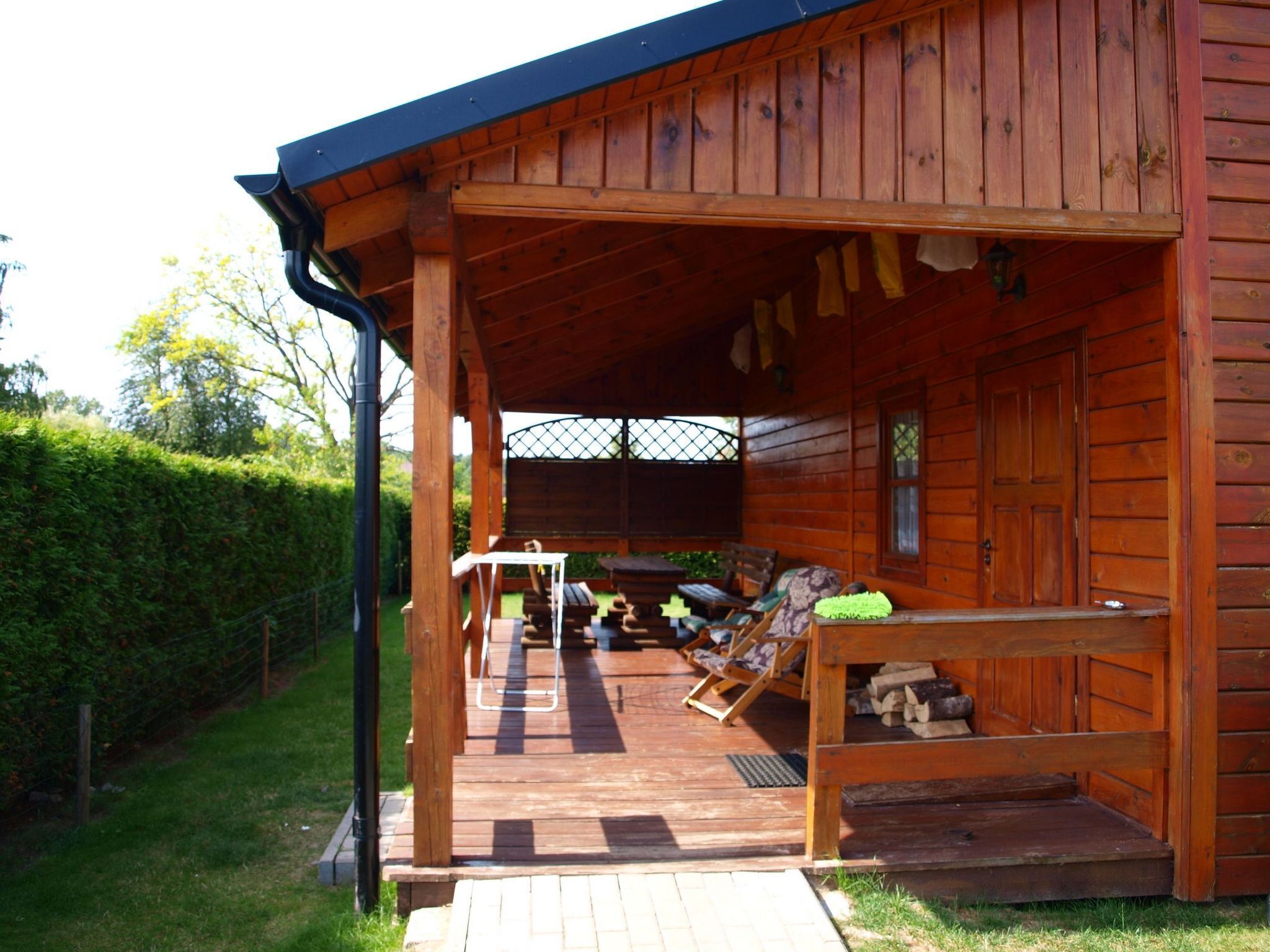 A wooden cabin with a covered porch, outdoor seating, and a firewood storage area.