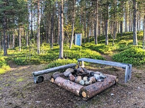 A forest clearing with a fire pit, logs, and a bench. - Kleines Ferienhaus in Arvidsjaur mit Sauna by Interhome (Arvidsjaur)