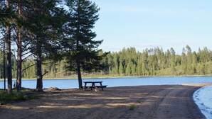 Una playa arenosa con una mesa de picnic y un banco, rodeada de árboles y un lago.