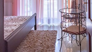Ein Schlafzimmer mit einem Bett, einem kleinen runden Tisch mit Stuhl und durchsichtigen Vorhängen.
