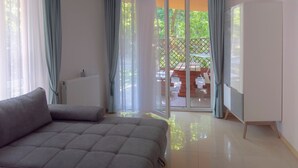 Ein modernes Wohnzimmer mit einem grauen Sofa, einem weißen Heizkörper und einer Glastür, die auf eine Außenpatio mit Tisch und Stühlen führt.