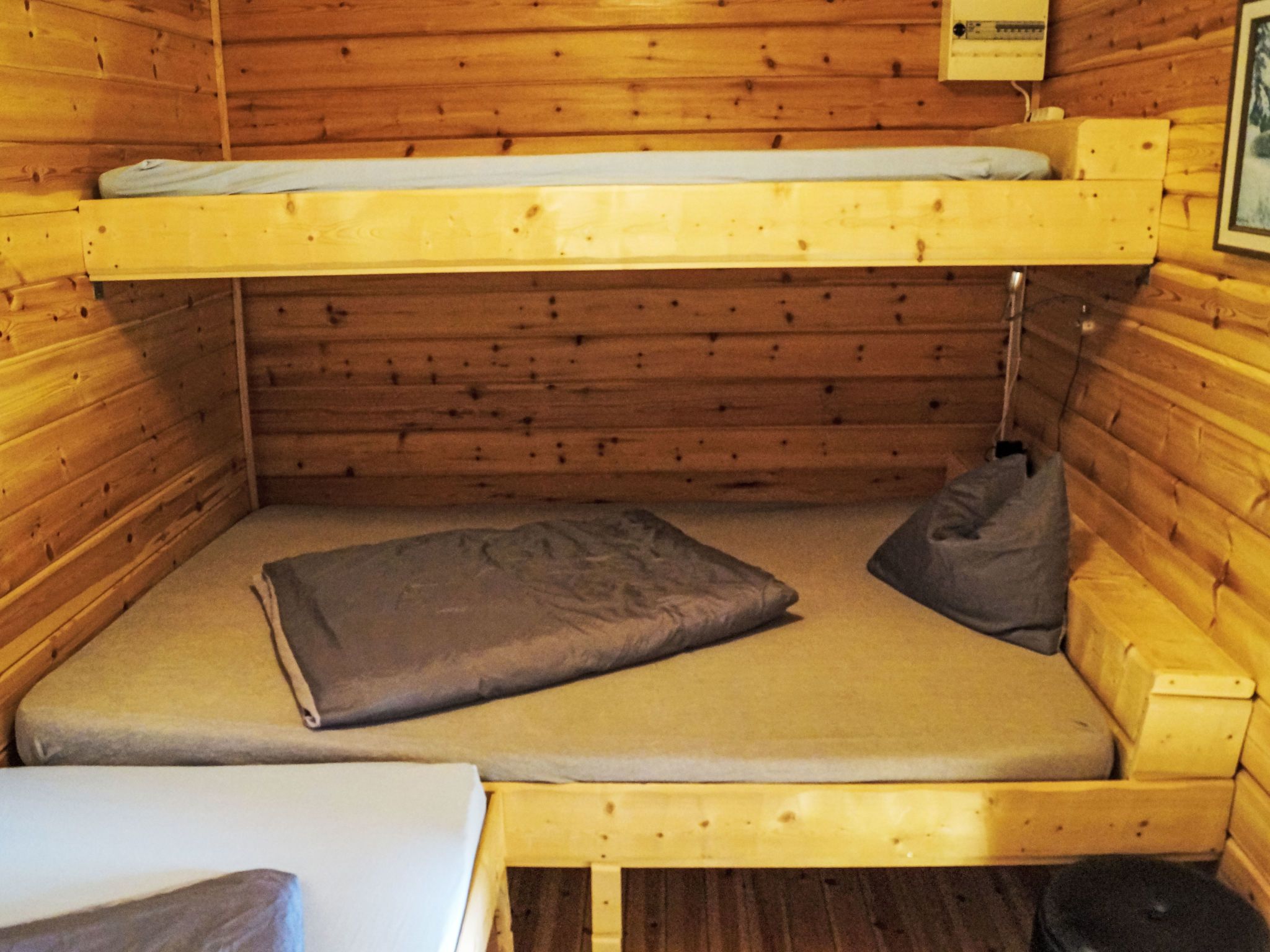 A bunk bed with a mattress and pillows, wooden walls, and a small table.