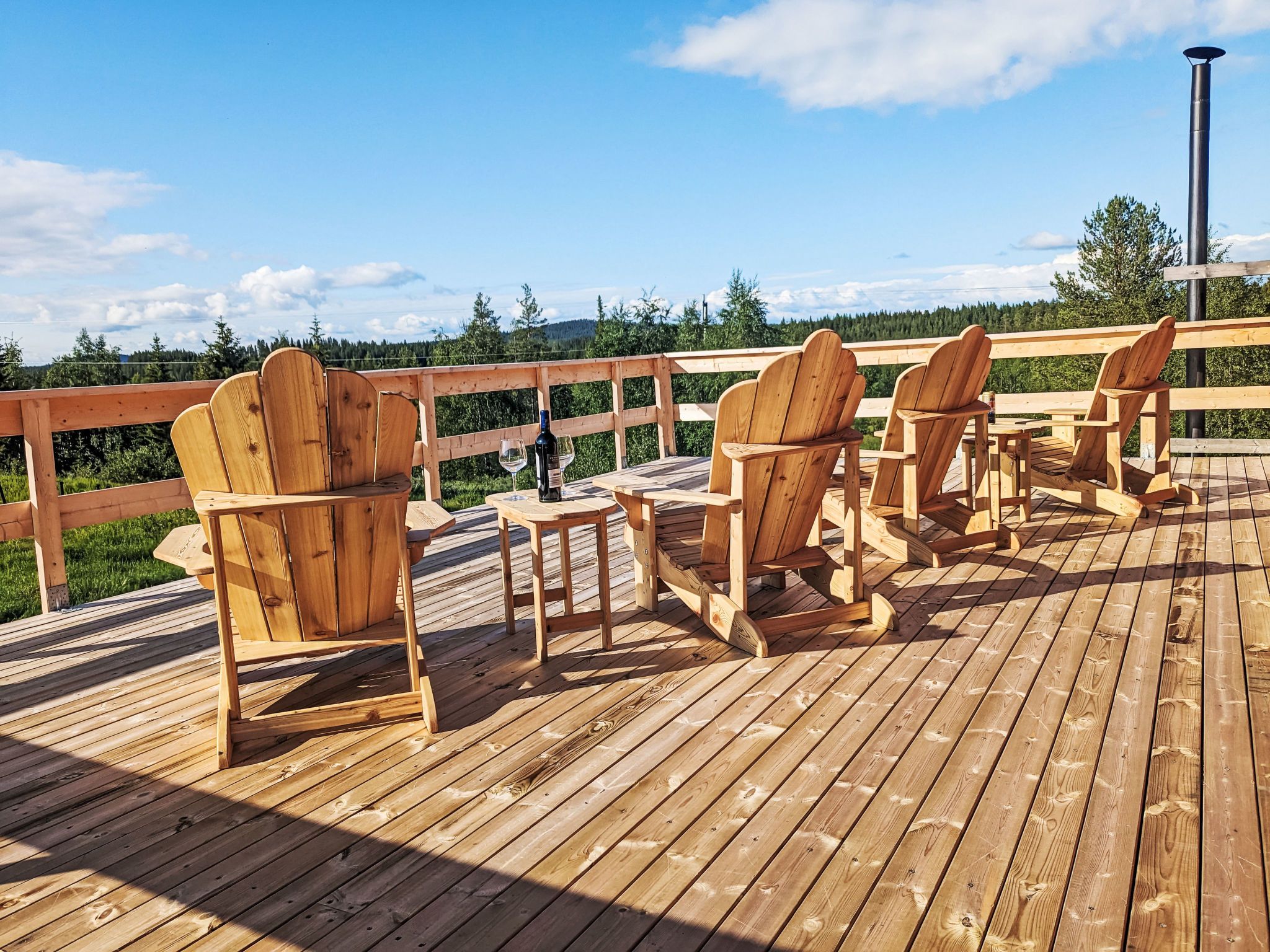 A wooden deck with Adirondack chairs and a table, overlooking a forested landscape.
