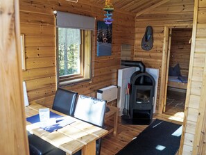L’intérieur d’un chalet en bois comprend une table à manger, des chaises, une cheminée et une fenêtre avec des rideaux.