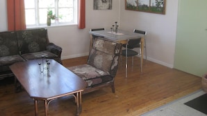 A living room with a wooden coffee table, a sofa, a dining table with chairs, and two paintings on the wall.