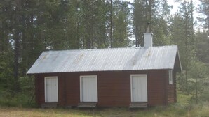 A small, single-story cabin with a metal roof and three white-framed windows.