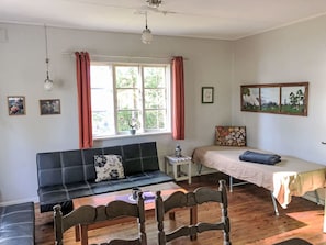 A room with a sofa, a bed, a small table, and a window with curtains.