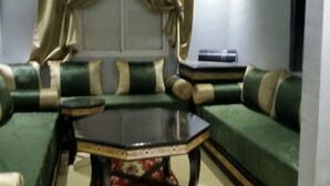 Een woonkamer met een groene bank, een salontafel met glazen blad en beige gordijnen.