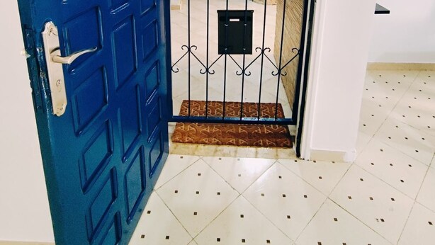 A blue door with a metal gate, a patterned rug, and a wall-mounted light fixture. - Wohnung "Loft in Tanger" by Interhome (Tanger)